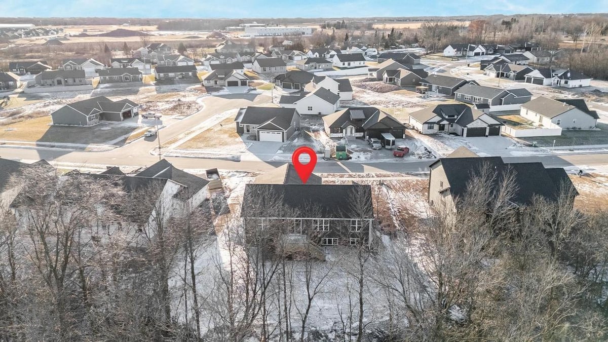 Drone view from behind of Fox Cities home with deck, wooded backdrop and nearby homes