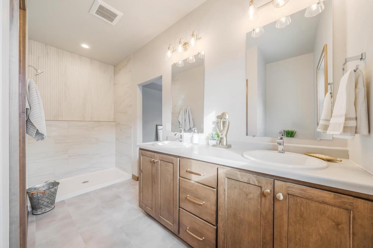 Fox Cities bathroom with double vanity, wood cabinetry, bright sconces, and tiled walk-in shower