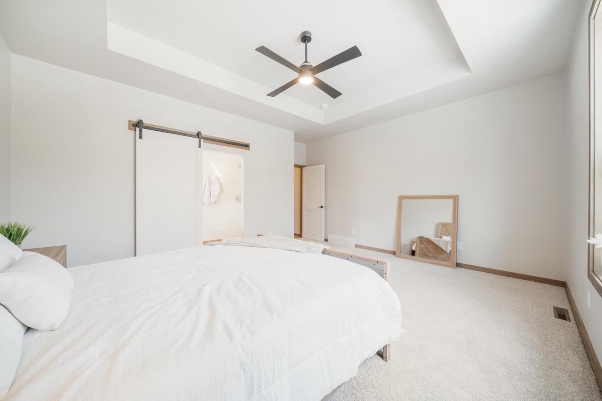 Fox Cities bedroom with light carpet, modern ceiling fan, barn door entry, and neutral walls