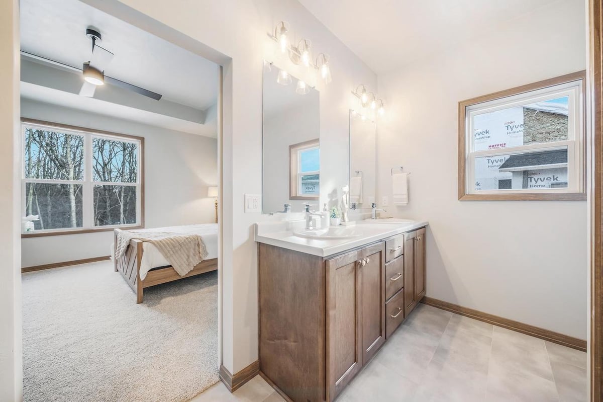 Fox Cities primary bath vanity with double sinks, wood cabinets, bright lighting, and bedroom view beyond