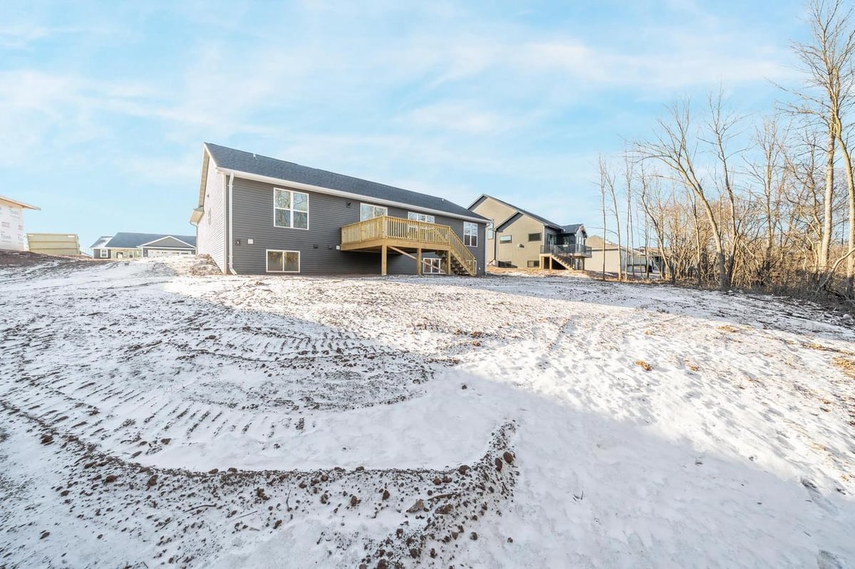 Rear exterior of a Fox Cities home with elevated deck, walkout basement windows, and snowy backyard