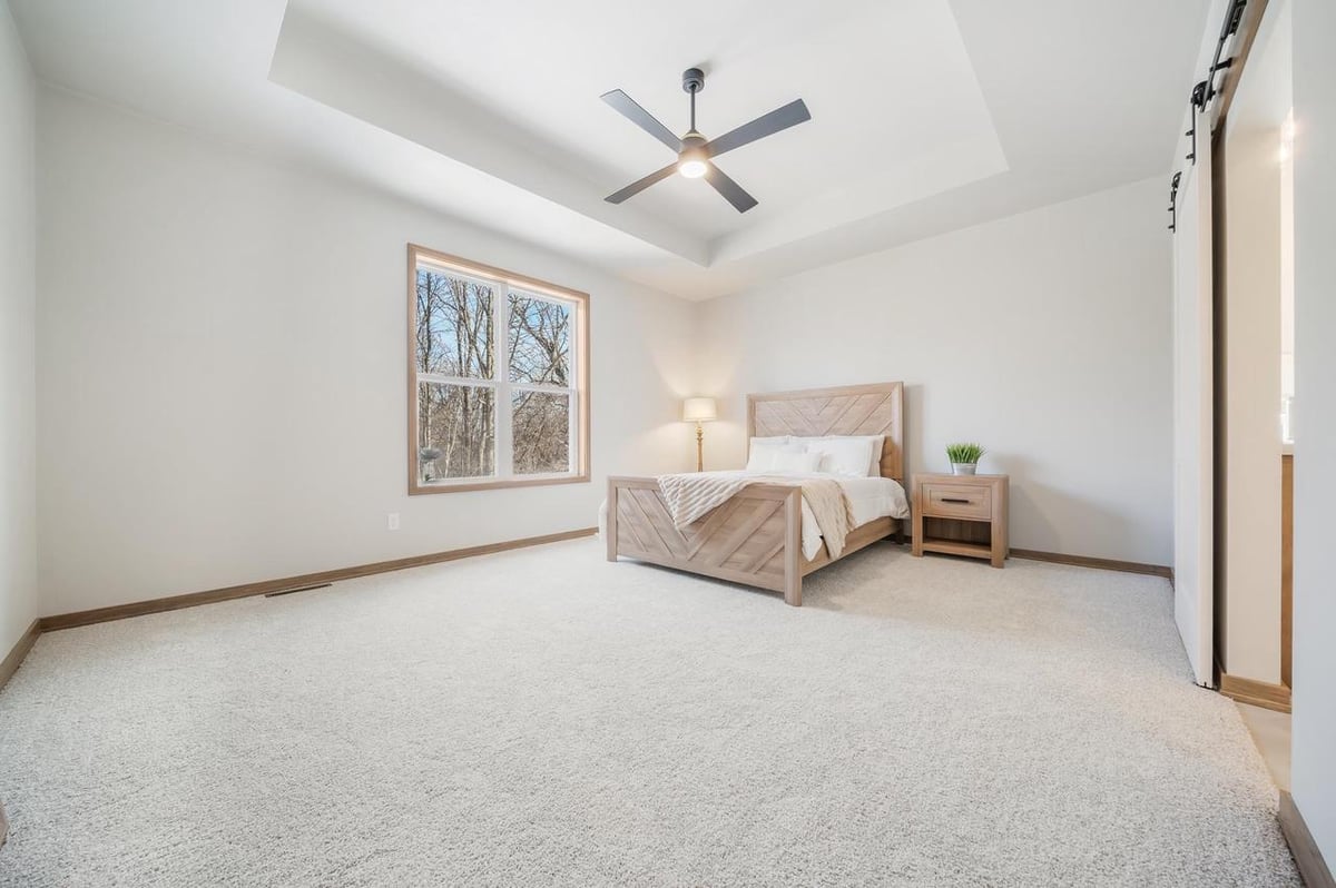 Spacious Fox Cities bedroom with tray ceiling, large window, and light wood bed frame