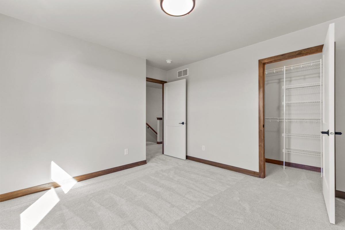 Bright carpeted bedroom with open closet and white doors in a custom home by Midwest Design Homes in De Pere, WI