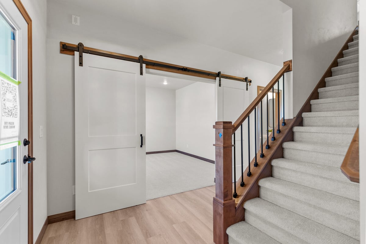 Open entryway with white barn doors and wood stairway in a Fremont, WI home by Midwest Design Homes