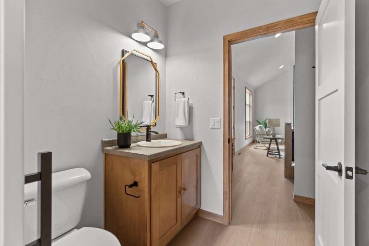 Half bathroom with wood vanity and gold-framed mirror in a Green Bay, WI custom home by Midwest Design Homes