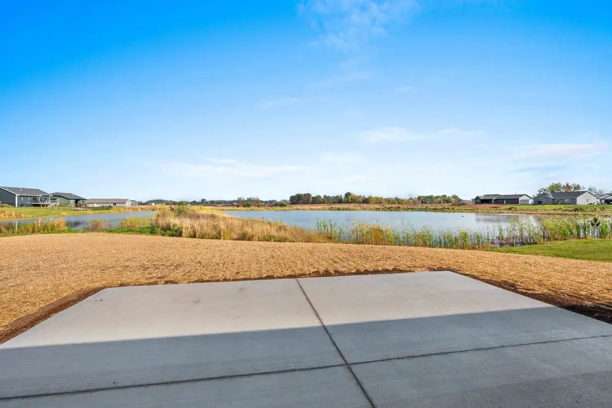 Backyard view of a waterfront property in the Fox Cities, featuring a concrete patio and scenic lake surrounded by natural grasses