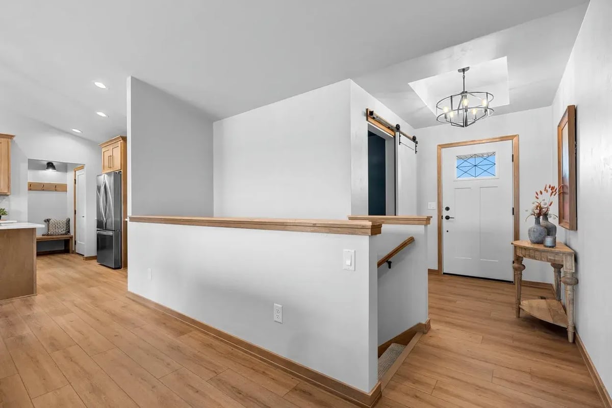 Bright Fox Cities home entryway with wood flooring, modern light fixture, barn door, and stairway leading to lower level