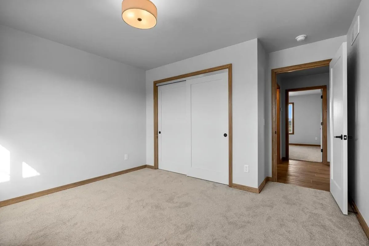 Bright bedroom with neutral carpet, double closet doors, and wood trim located in the Fox Cities