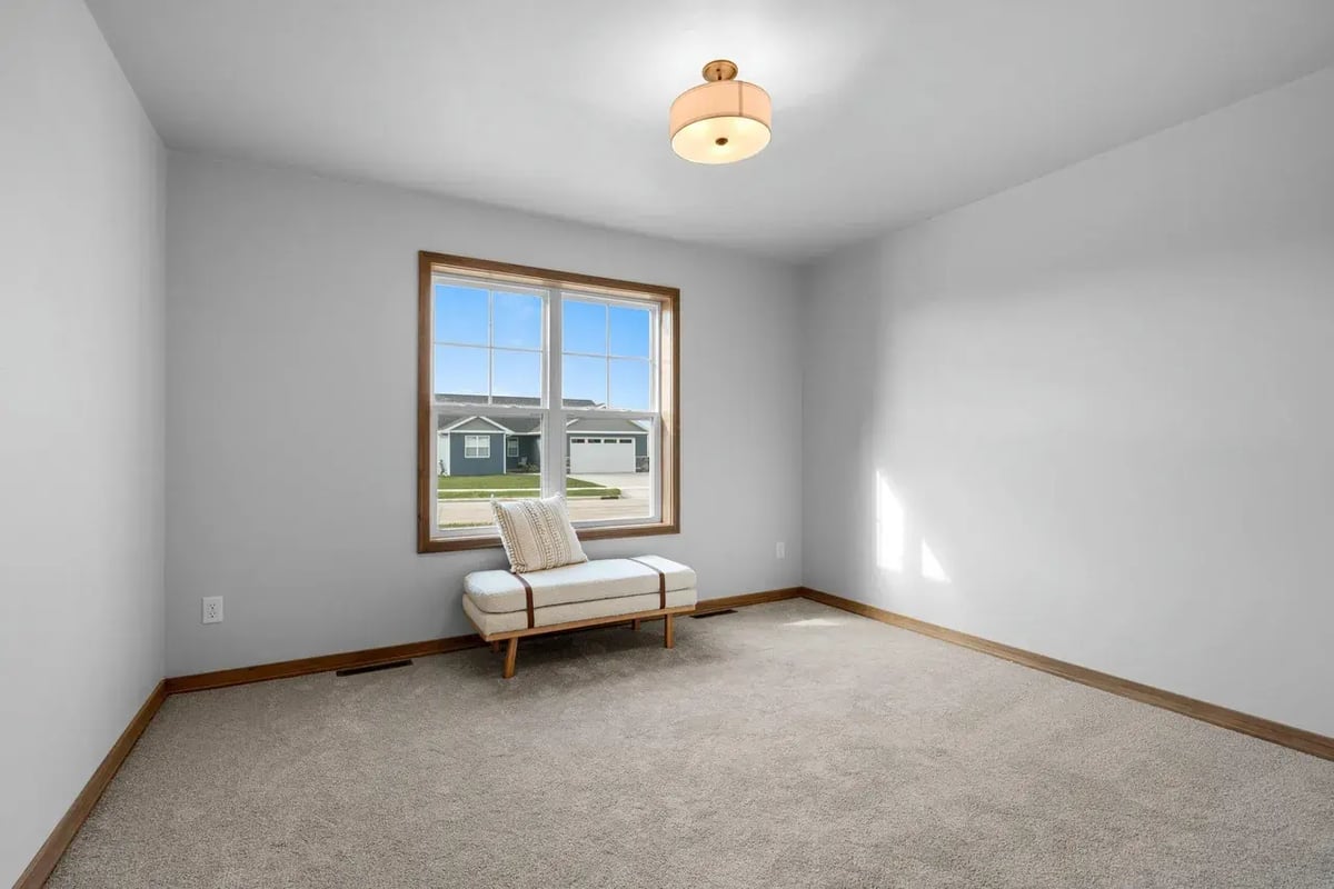 Bright carpeted room with a large window, wood trim, and accent bench, located in the Fox Cities