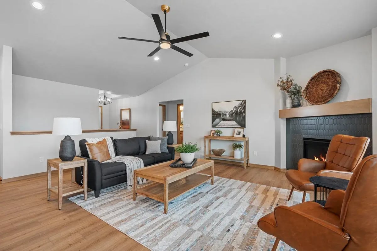 Cozy Fox Cities living room with fireplace, black sofa, leather chairs, and modern ceiling fan on wood flooring