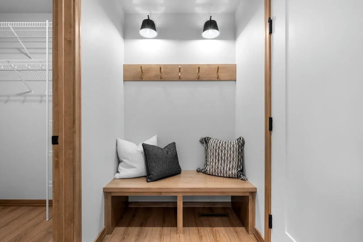 Cozy mudroom bench with hooks, pillows, and overhead lighting in a modern Fox Cities home