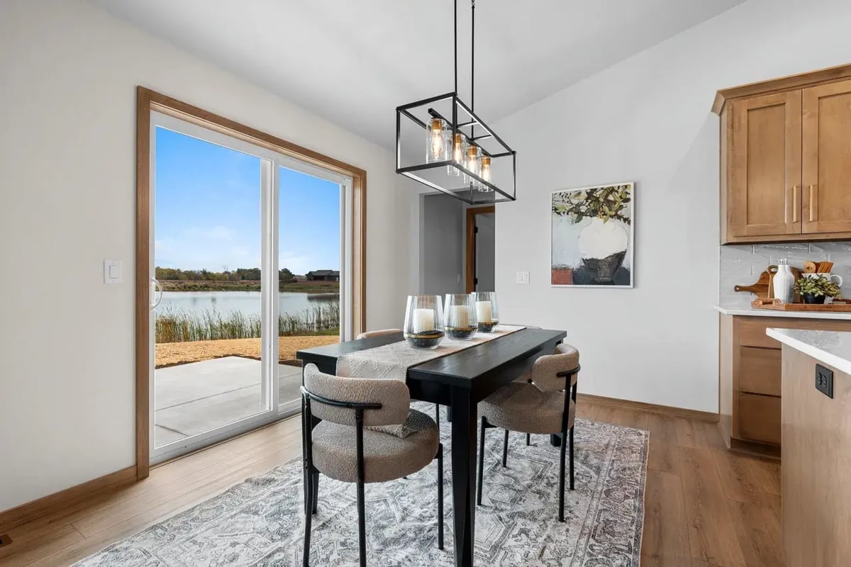 Dining area in the Fox Cities with modern chandelier, black table, and patio doors overlooking a scenic pond and natural landscape