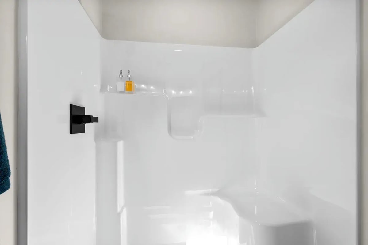 Fox Cities bathroom shower with a built-in seat, black matte fixture, and soap dispensers on a molded corner shelf