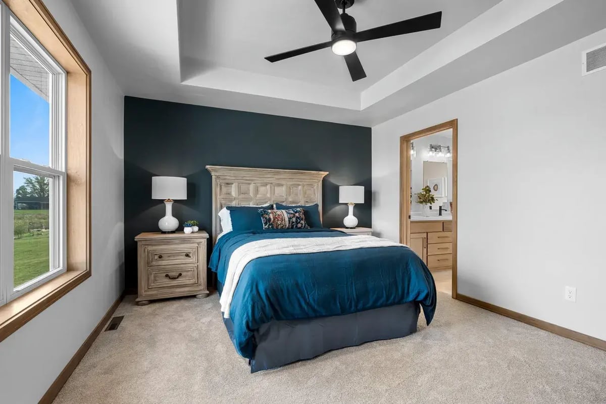 Fox Cities bedroom with tray ceiling, bold accent wall, wood furnishings, and natural light from a large window