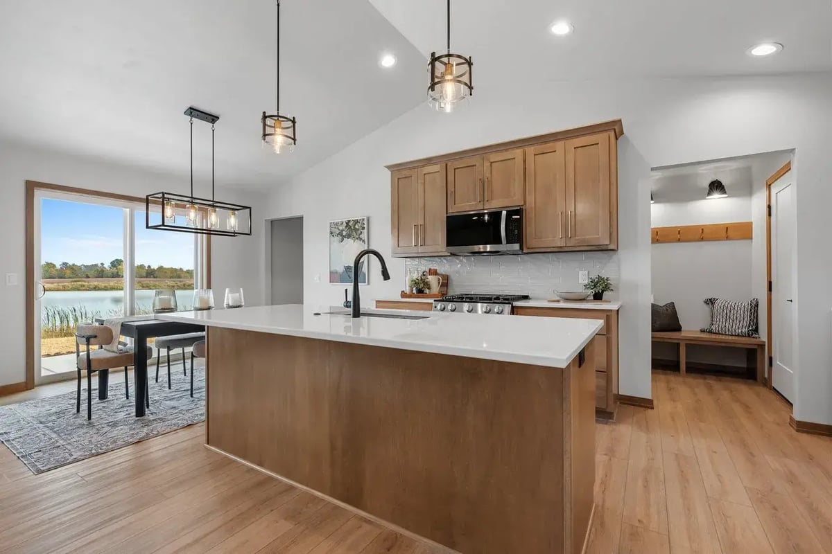 Fox Cities kitchen with wood cabinets, white quartz island, black fixtures, modern lighting, and scenic dining area by a large window