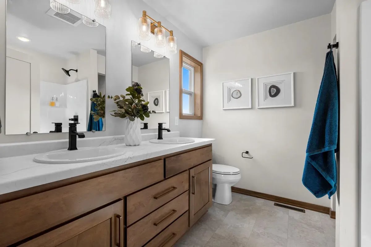 Modern Fox Cities bathroom featuring a double vanity with wood cabinetry, black fixtures, and decorative lighting above dual mirrors