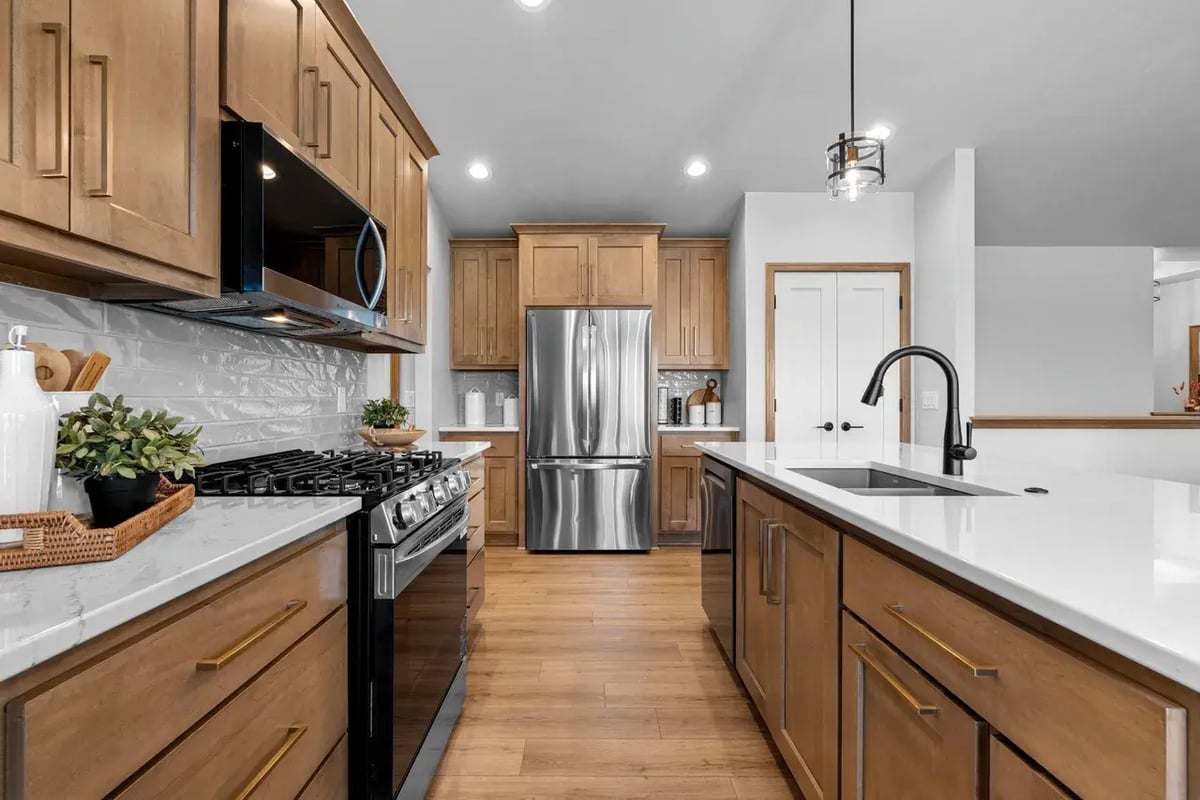 Modern Fox Cities kitchen with stainless steel appliances, wood cabinetry, white countertops, and a large island with black faucet