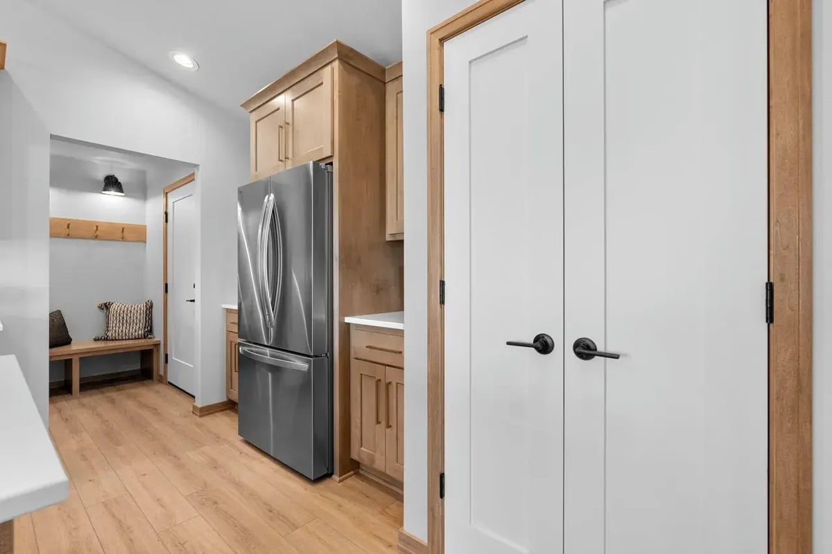 Modern kitchen and mudroom with wood floors, stainless steel fridge, and built-in bench, located in the Fox Cities