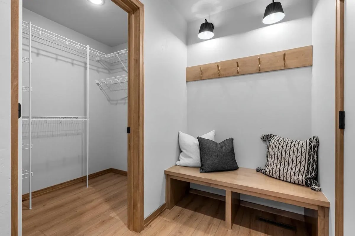Mudroom with wood bench, throw pillows, coat hooks, and adjacent walk-in closet with shelving, located in the Fox Cities