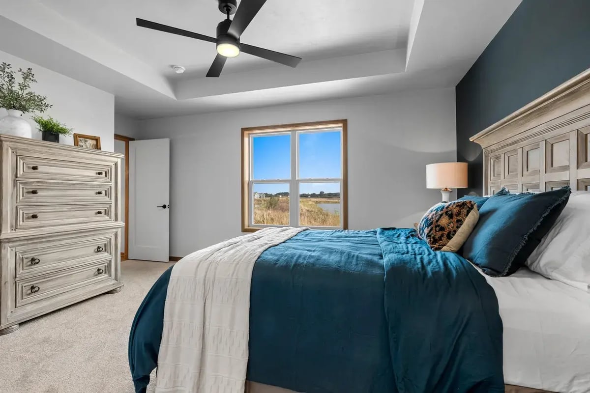 Primary bedroom in the Fox Cities with tray ceiling, large window with pond view, and stylish wood furniture and teal bedding