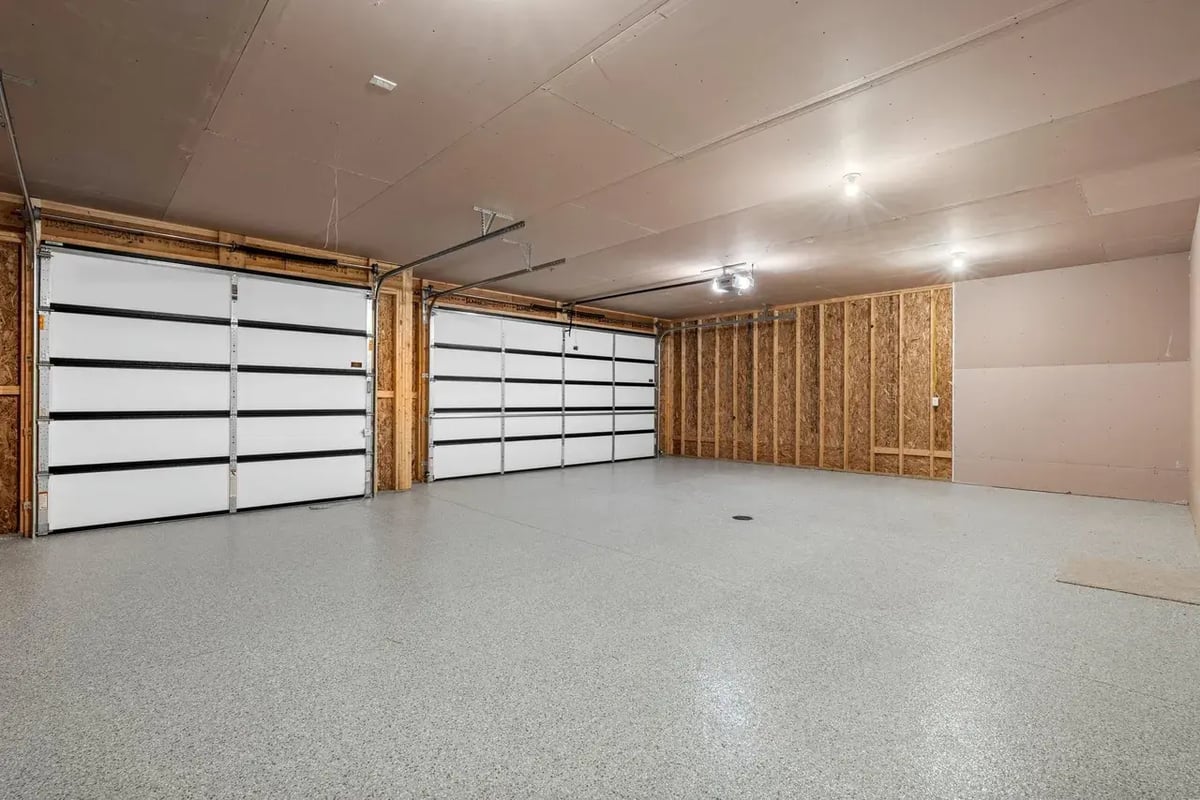 Spacious three-car garage in the Fox Cities with finished floors, exposed framing, and dual white overhead doors