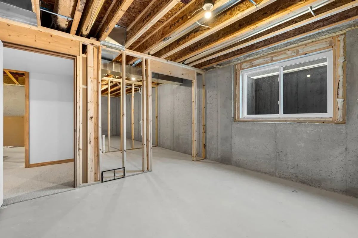 Unfinished basement in a Fox Cities home with exposed framing, concrete walls, and a large window providing natural light