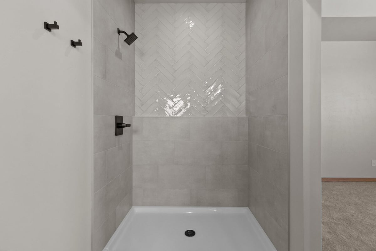Modern walk-in shower featuring herringbone tile by Midwest Design Homes in Lawrence, WI