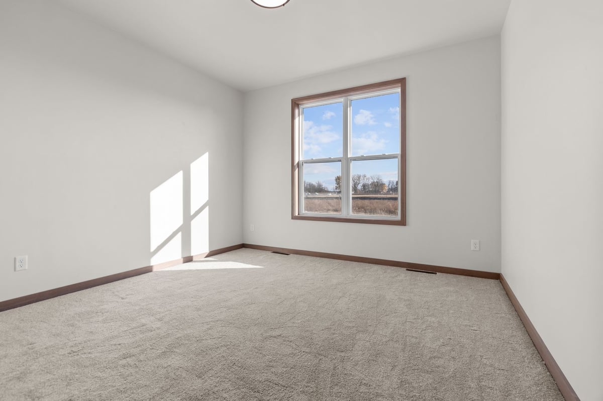 Empty bedroom with carpeted floor and large window letting in natural light, located in the Fox Cities