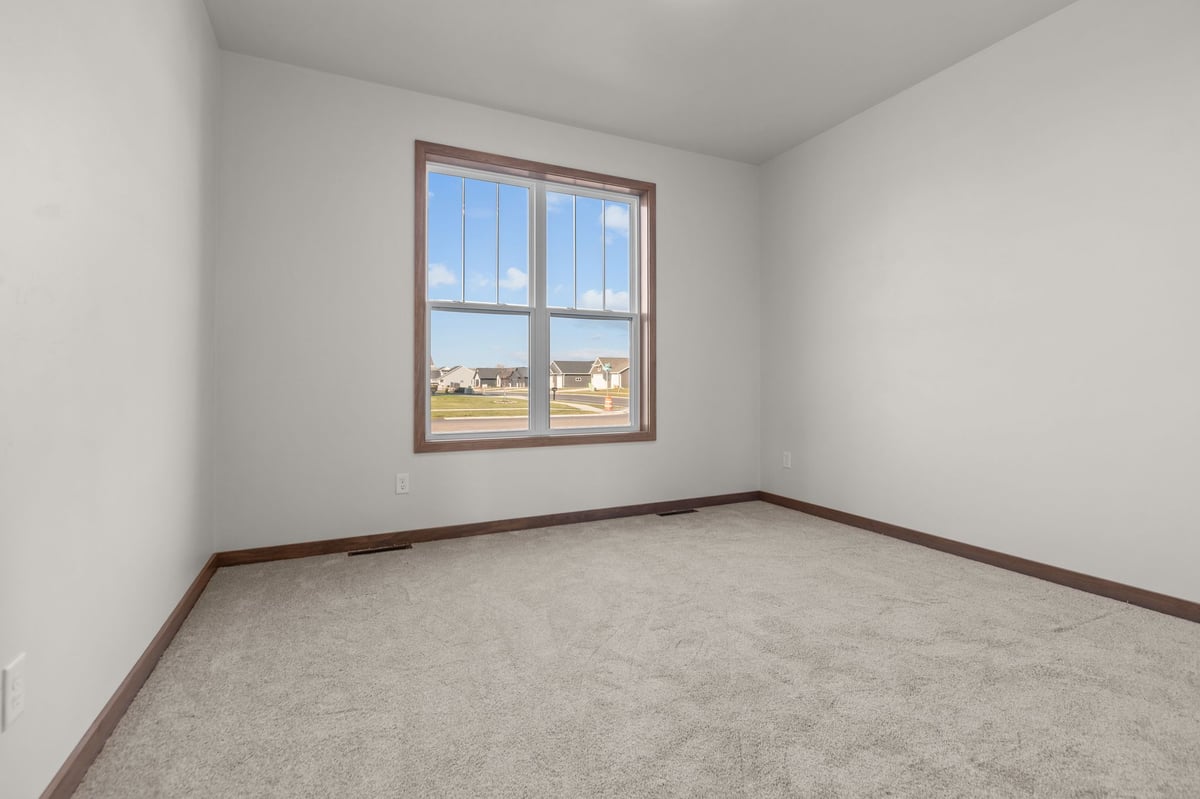 Empty bedroom with carpeted floors, neutral walls, and a large window, located in the Fox Cities