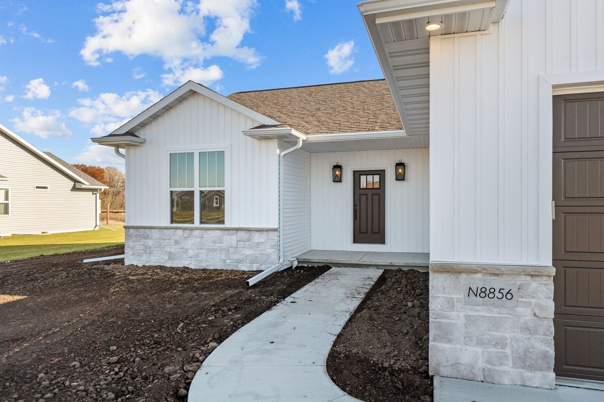 Front entry of a newly built white home with covered porch and concrete walkway, located in the Fox Cities