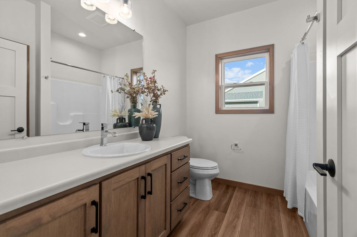 Hall bathroom with wood vanity, white countertop, tub shower, and window, located in the Fox Cities