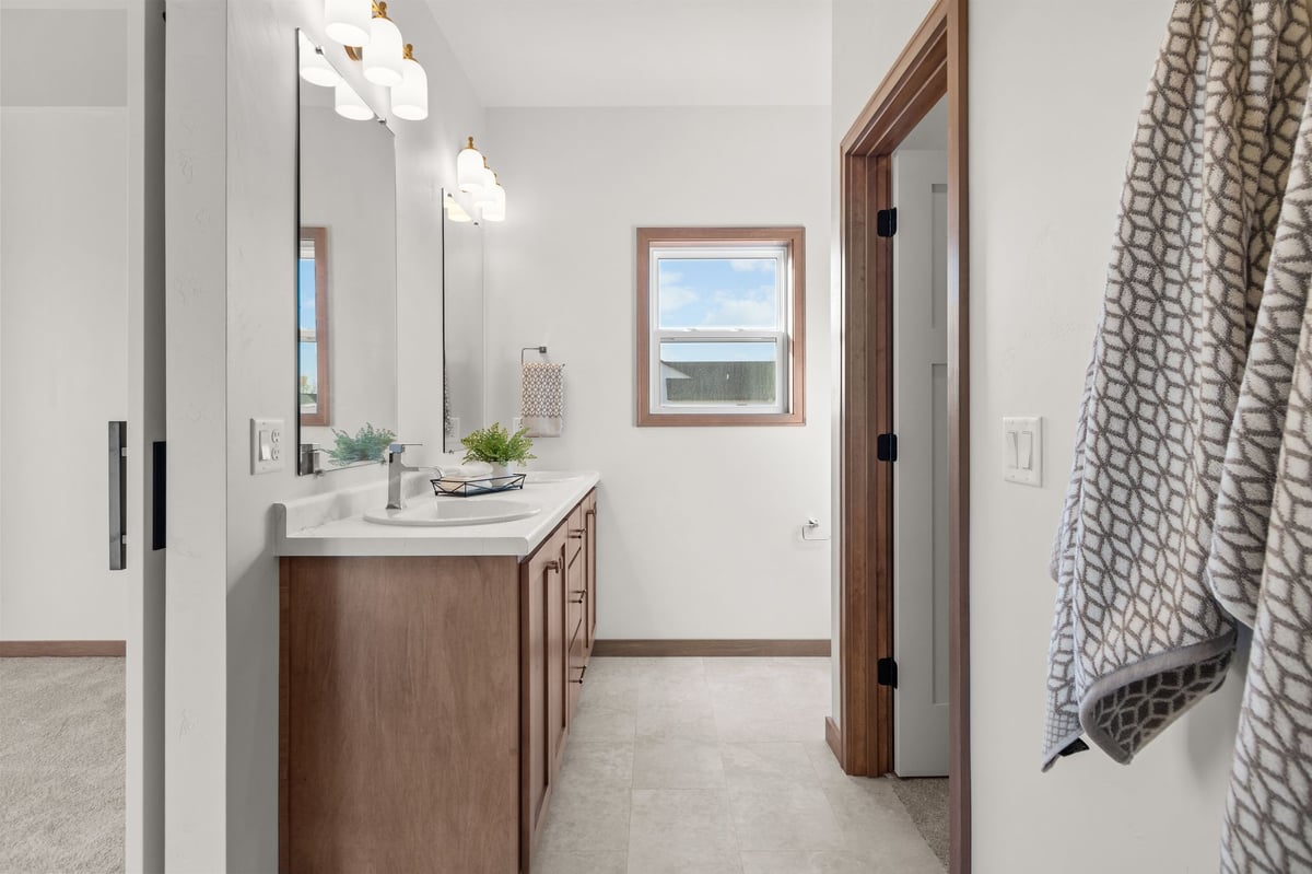 Primary bathroom with wood vanity, white countertop, modern lighting, and window, located in the Fox Cities