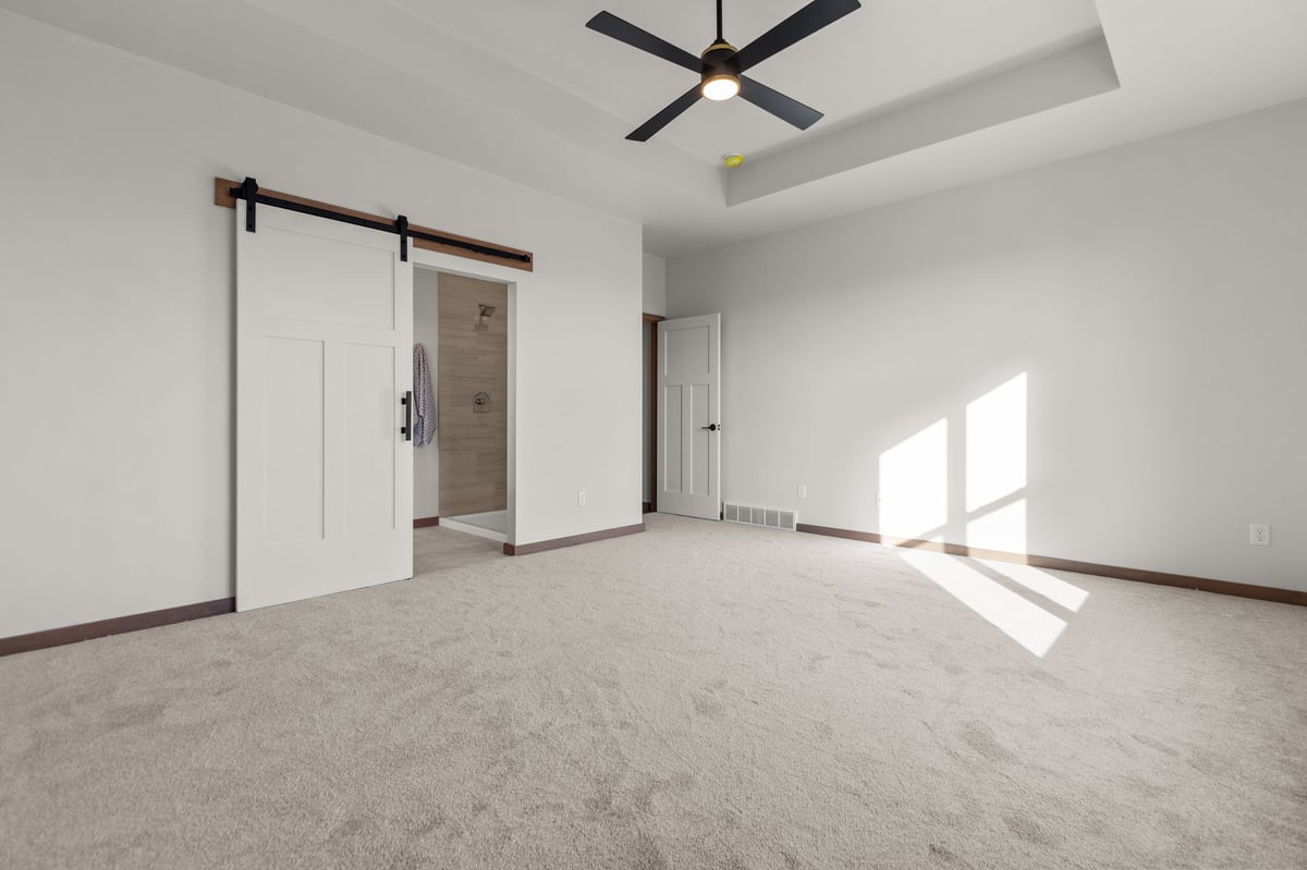 Spacious primary bedroom with tray ceiling, ceiling fan, and sliding barn door, located in the Fox Cities