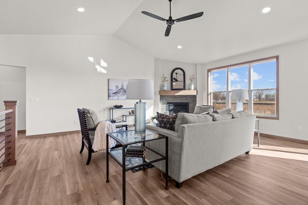 Staged great room with fireplace, ceiling fan, and large windows, located in the Fox Cities