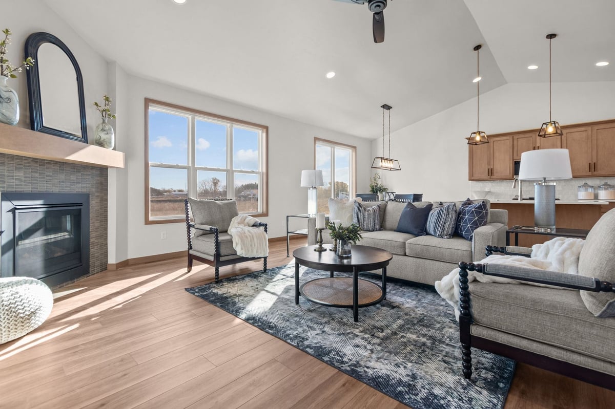 Staged great room with fireplace, seating area, large windows, and open kitchen, located in the Fox Cities