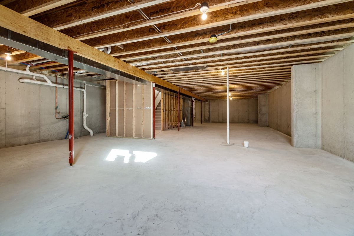 Unfinished basement with concrete floors, exposed beams, support columns, and utility rough-ins, located in the Fox Cities