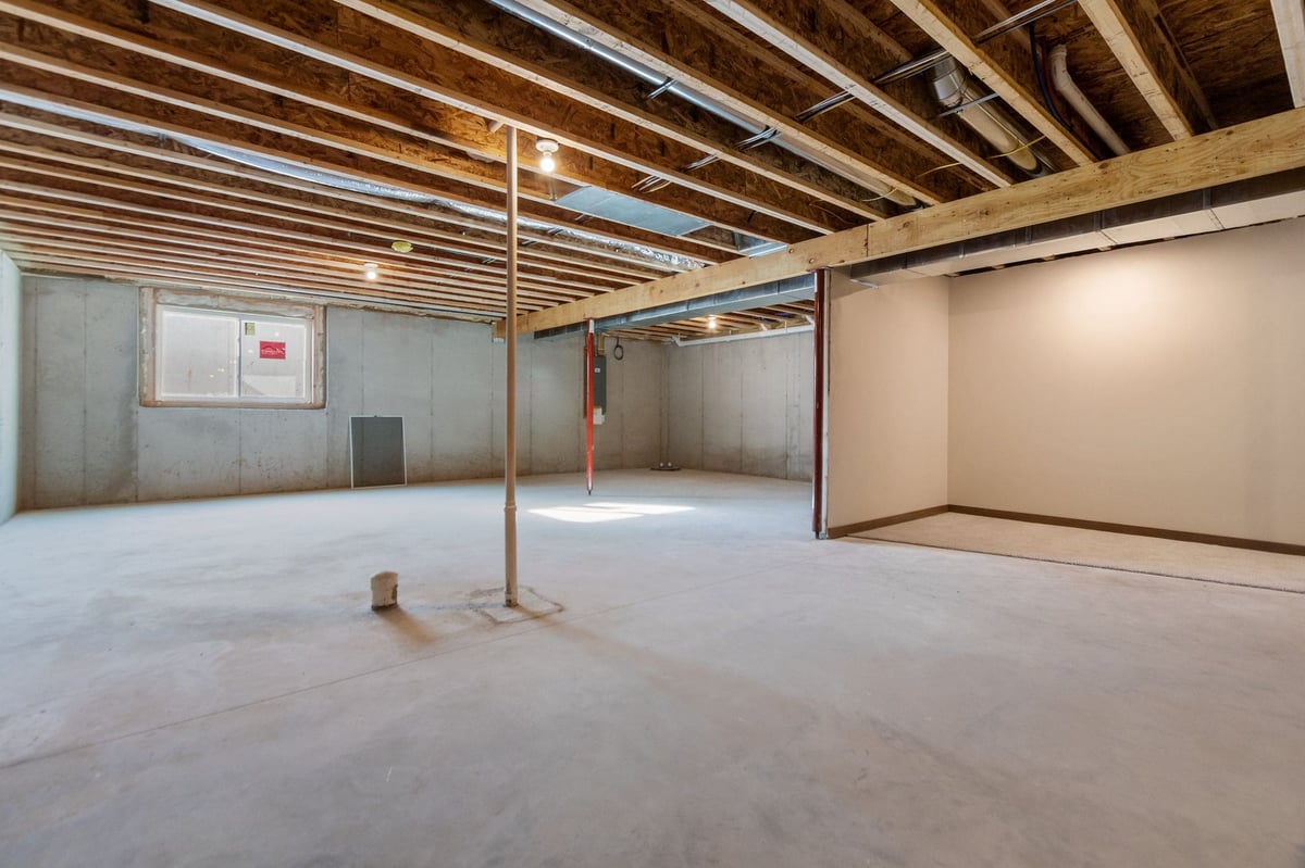Unfinished basement with open layout, exposed beams, concrete floors, and partial finished area, located in the Fox Cities