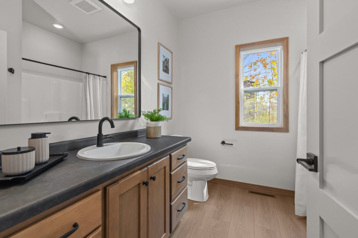 Modern bathroom with large mirror and natural wood tones by Midwest Design Homes in Appleton, WI