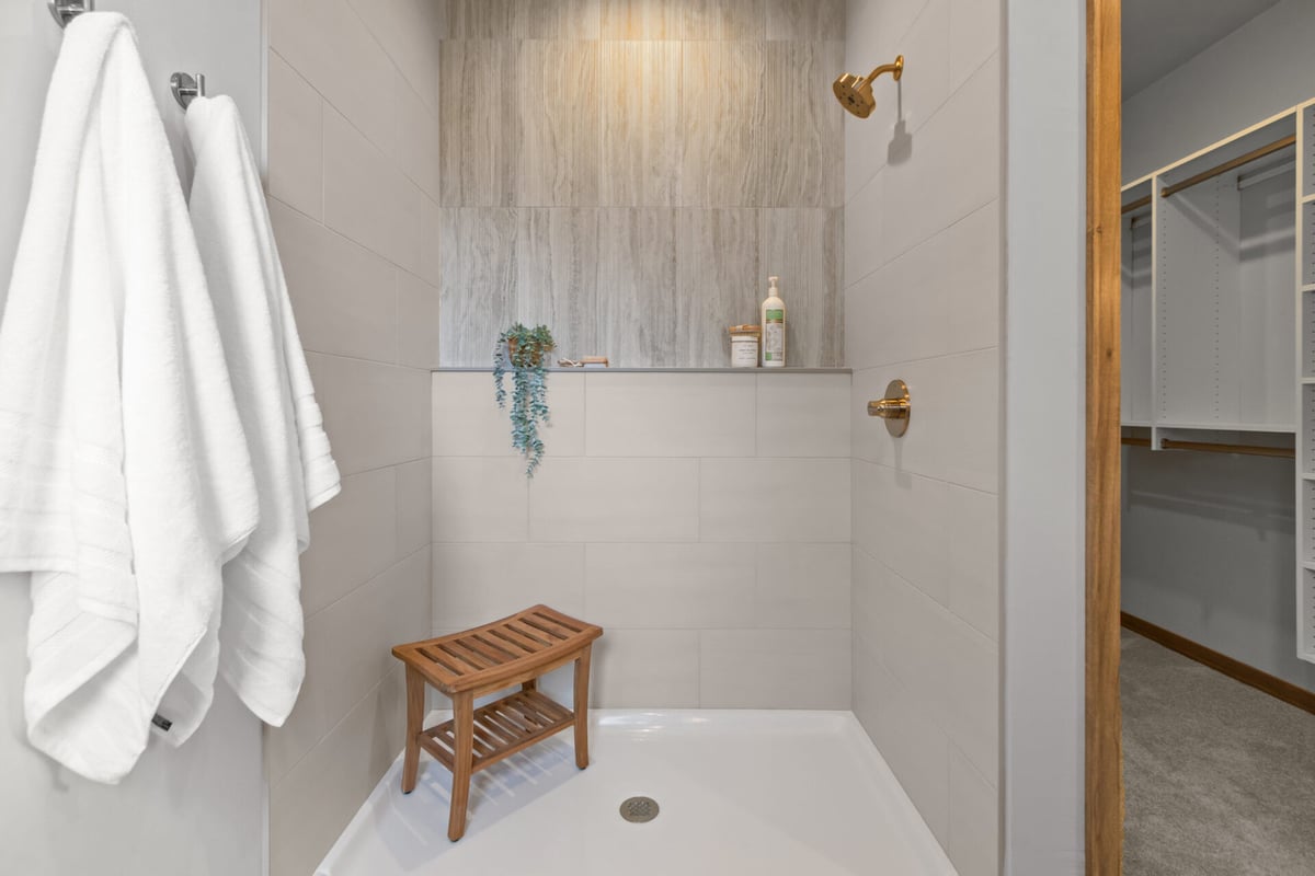 Walk-in shower with wood bench and gold fixtures in custom home by Midwest Design Homes in Kaukauna, WI