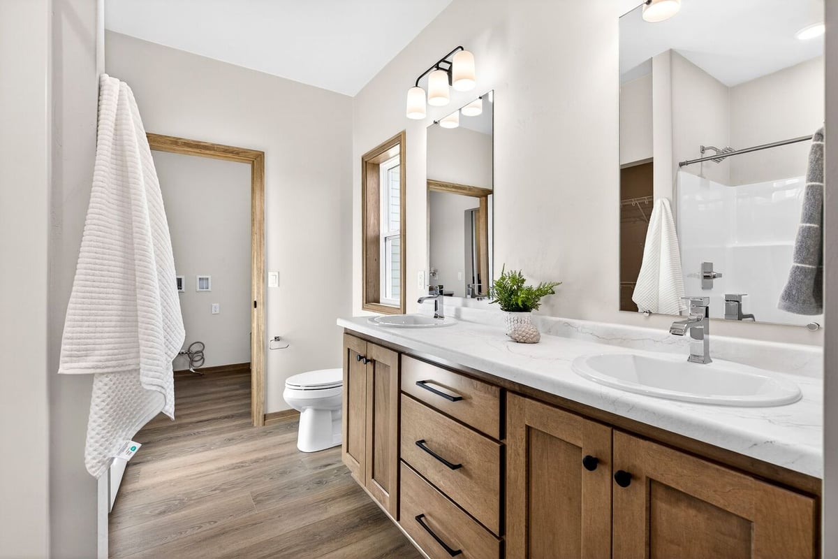 Bright bathroom with double vanity, wood cabinetry, quartz counters, and walk-in shower in a Fox Cities home