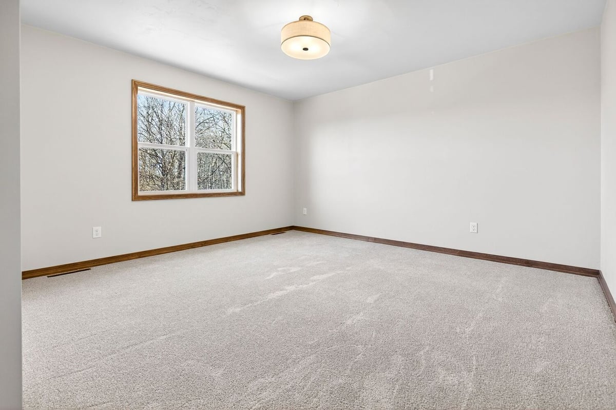 Bright carpeted bedroom with window, neutral paint, wood trim, and modern ceiling light in the Fox Cities