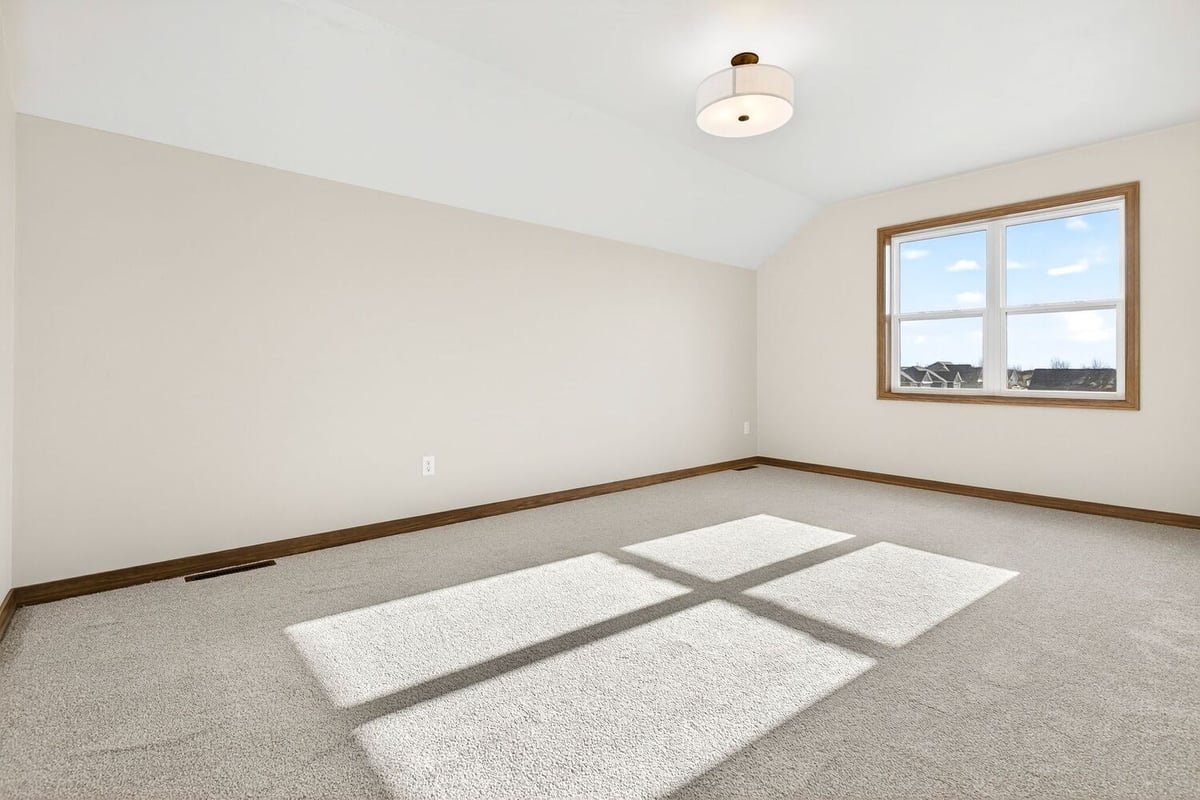 Bright empty bedroom with carpet, neutral walls, and large window letting in sunlight in a Fox Cities home