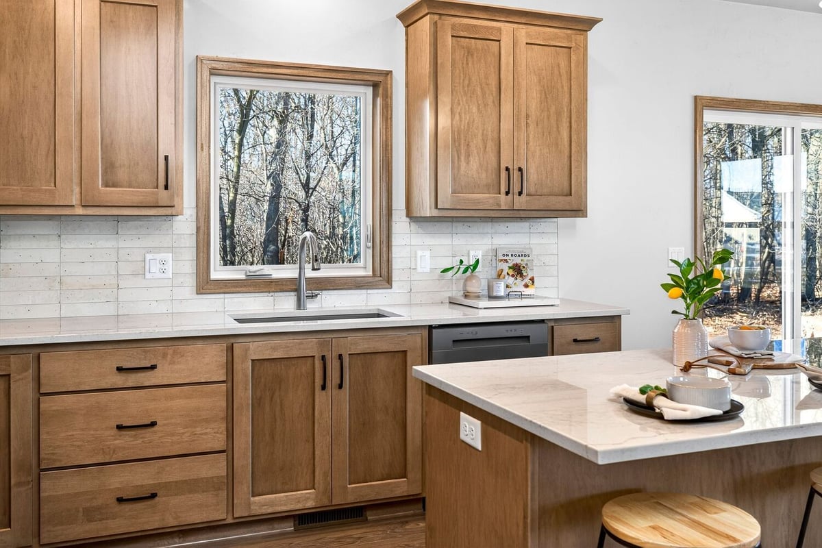 Bright kitchen with warm wood cabinets, white backsplash, quartz island, and window views in a newly built Fox Cities home