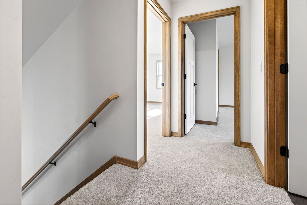 Carpeted upstairs hallway with stair railing and multiple doorways in a Fox Cities home