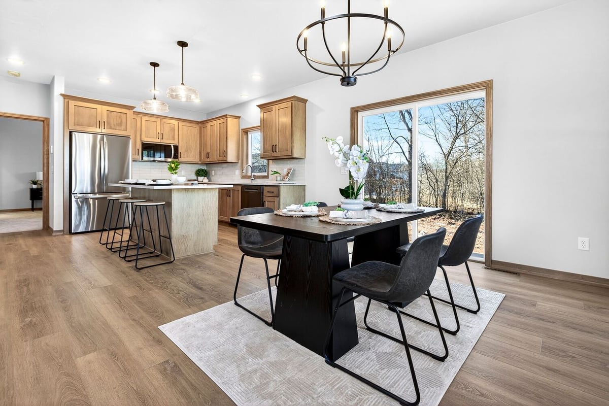 Dining area with black table, modern chandelier, and wooded backyard views in a Fox Cities home