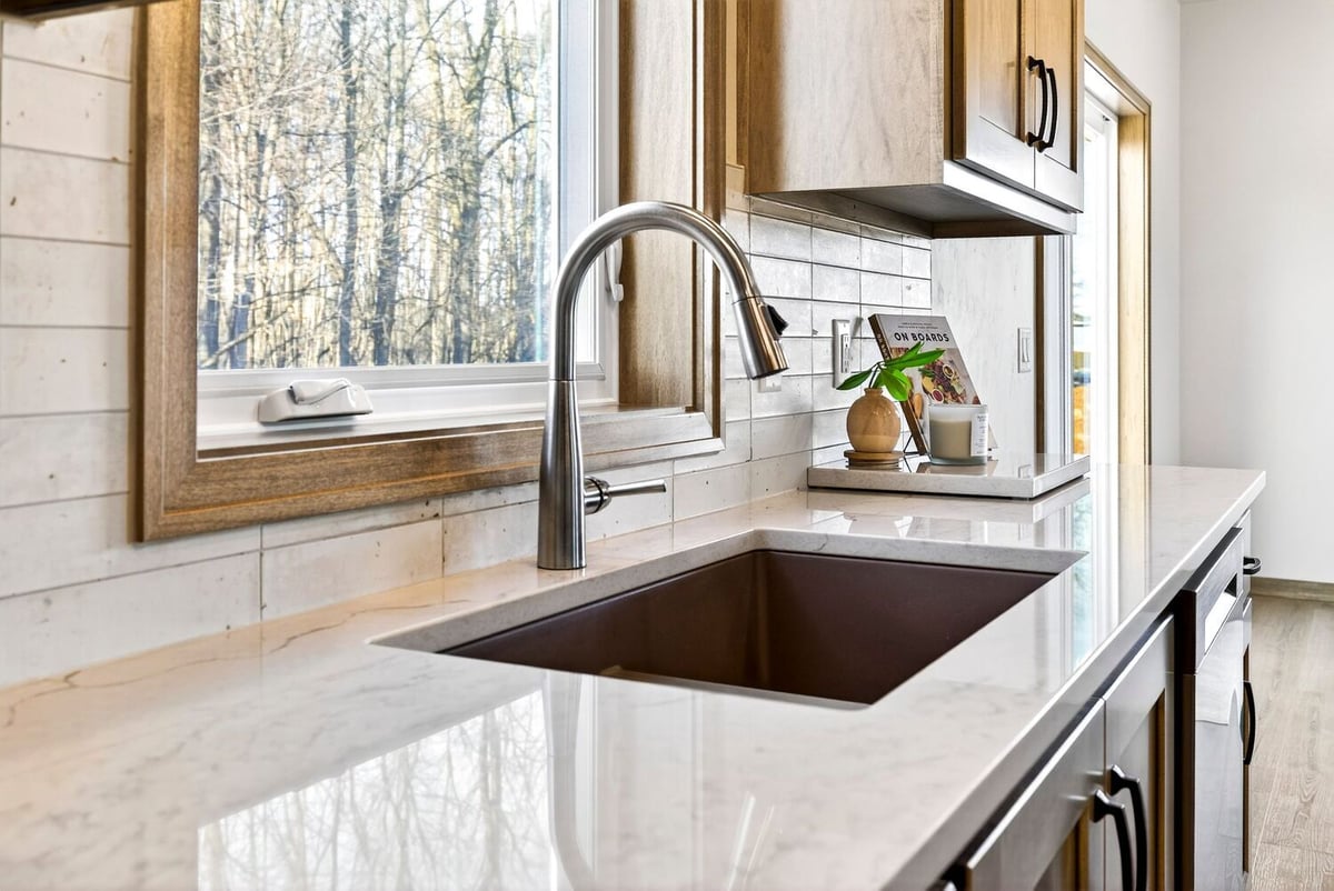 Kitchen sink close-up with quartz countertops, modern faucet, and wood cabinets beside a window in a Fox Cities home