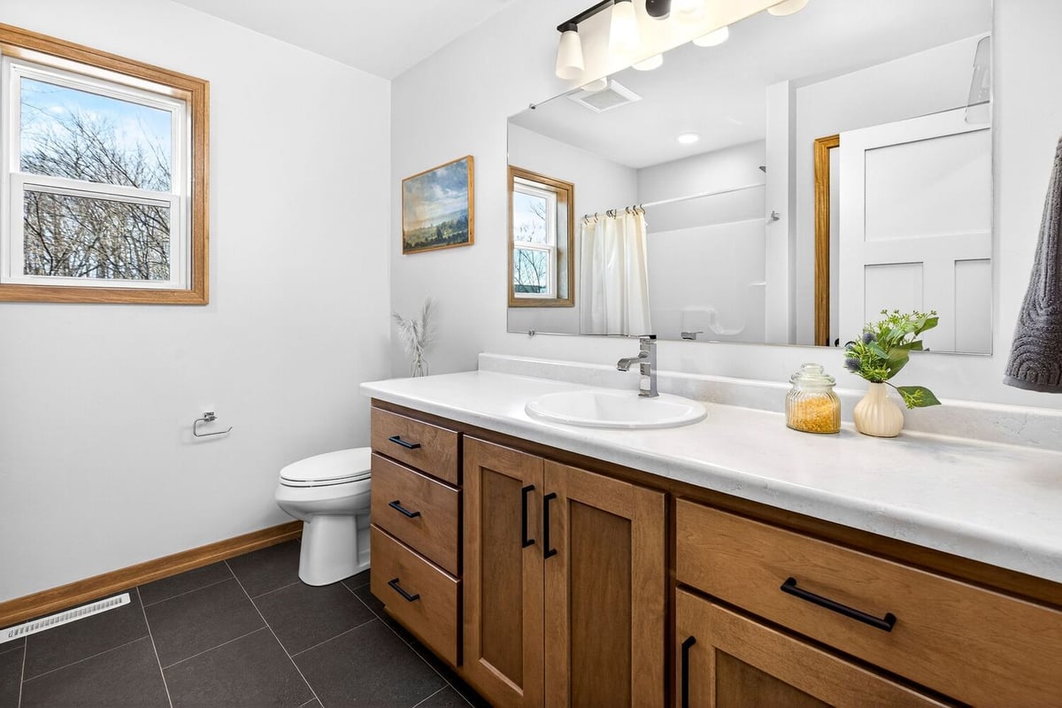 Modern bathroom with wood vanity, white countertop, large mirror, and tub shower in a Fox Cities home