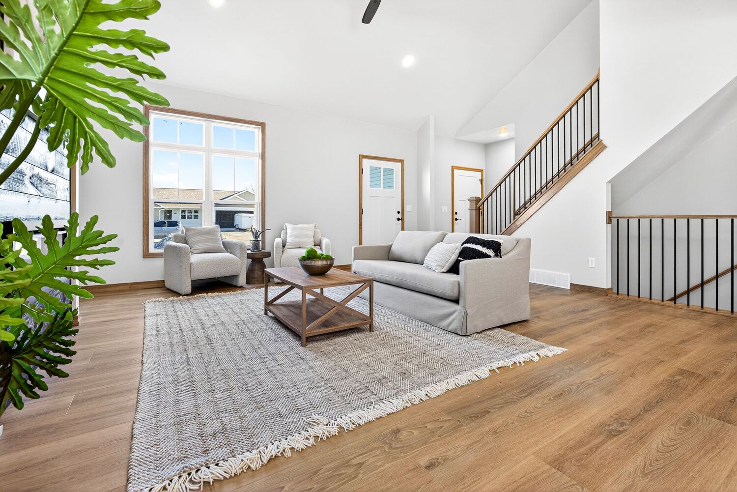 Open living room with staircase, neutral furnishings, wood floors, and airy layout in a Fox Cities new build