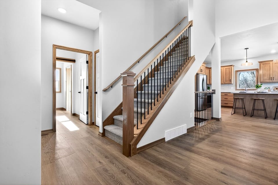 Open stairway with wood railing and black balusters leading upstairs in a bright Fox Cities home with hardwood floors and views into kitchen