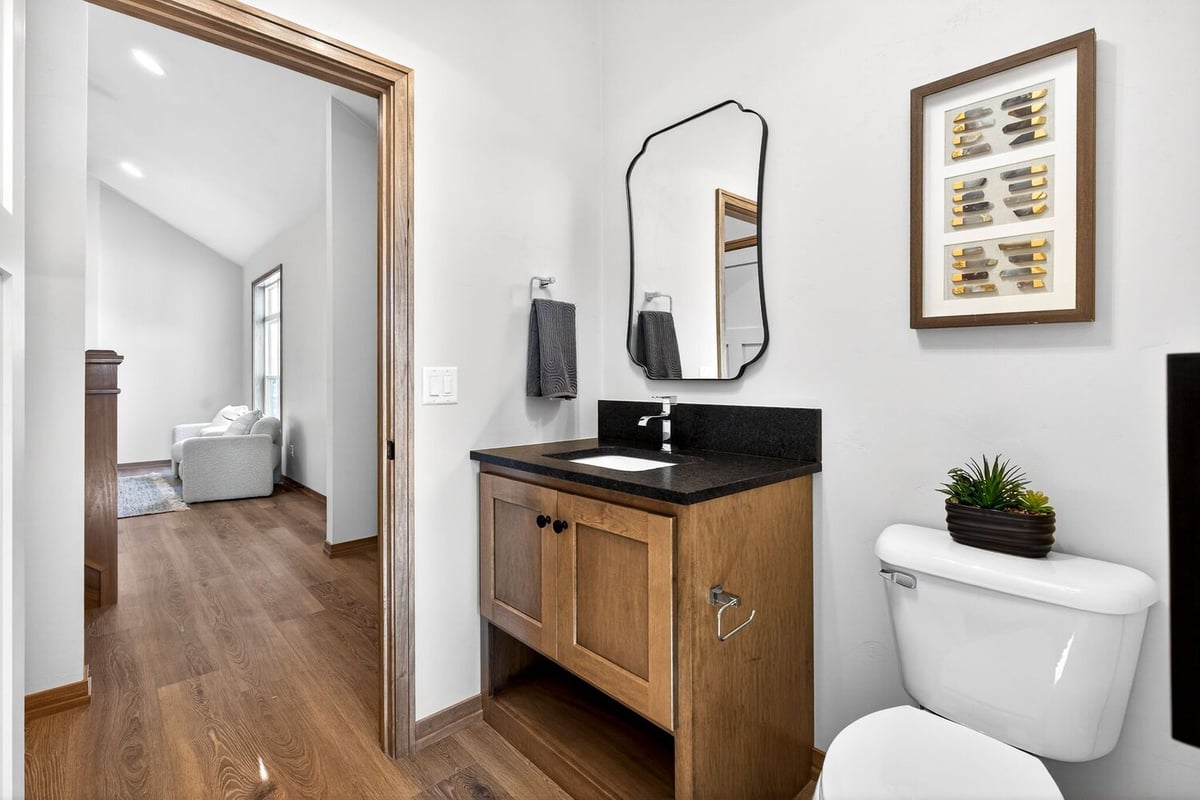 Powder room with wood vanity, black countertop, modern mirror, and toilet in a Fox Cities home
